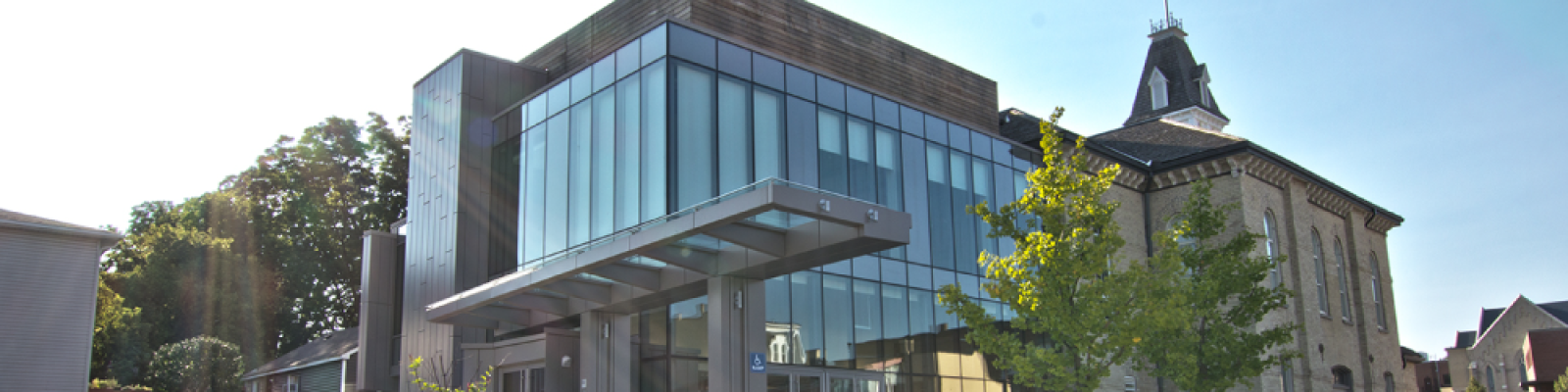 Modern glass building with a historic structure, under a clear sky.