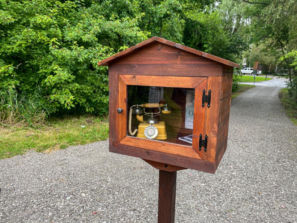 Wooden box with a vintage phone inside, by a gravel path and greenery.